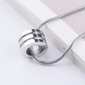 Macro shot of silver cylindrical pendant with grooves on a sleek snake chain