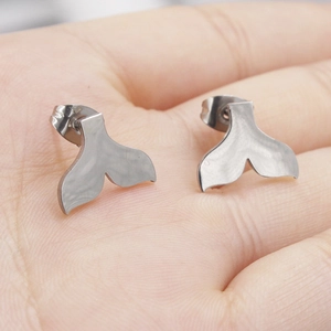 Macro view of mirror-polished stainless steel mermaid tail studs held on a palm