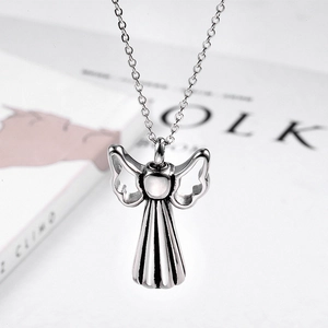 Polished stainless steel angel wing pendant necklace displayed on a magazine background