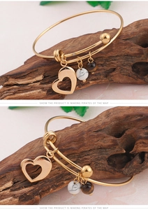 Détail d'un bracelet doré avec pendentif cœur, perle en marbre blanc et pierre œil de tigre