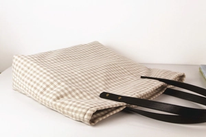 Detailed shot of beige gingham fabric and black leather handles with golden rivets