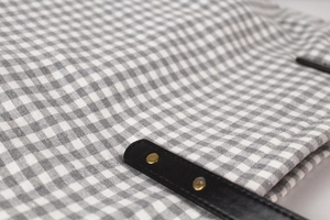 Close-up of checkered cotton bag with black leather handle and golden metal rivets