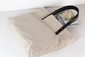 Detail of checkered canvas tote bag with black leather straps and gold rivets