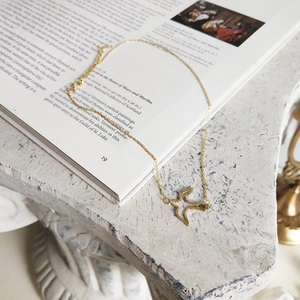 Detailed view of a gold swallow pendant necklace on a decorative art book background