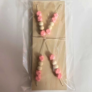 Detail of macaron pink and beige beads with cotton rope on a light wood shelf