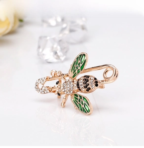 Detail of bee brooch featuring gold metal, green enamel wings, and sparkling rhinestones