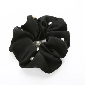 Détail d'un chouchou en satin noir orné de perles blanches sur fond blanc impeccable