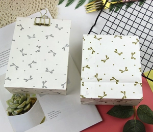 Detail view of bow pattern paper gift bags with decorative gold clips and greenery