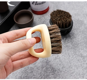 Detail of a handheld boar bristle beard brush with a beige handle for male grooming