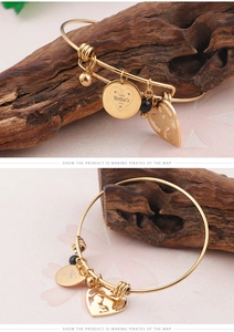 Detail of gold open bangle with Mother's Day charms and heart silhouette pendant