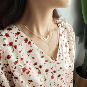 Detail of layered gold double-strand necklace with geometric pendant and long tassel on model