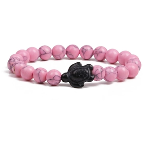 Macro shot of pink patterned beads and a black sea turtle charm on a beaded bracelet