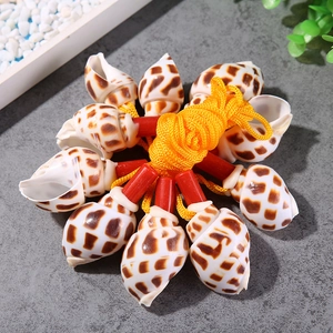 Close-up of spotted conch shell whistles connected by a yellow nylon cord on a stone surface