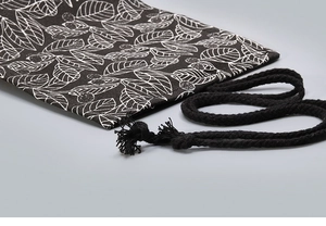 Detailed close-up of a black canvas drawstring bag featuring white leaf patterns and cords