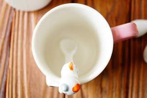 Close-up of a hand-painted ceramic cat-shaped stirring spoon resting in a mug