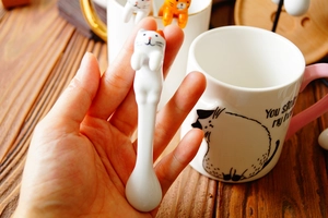 Close-up of a hand holding a white ceramic cat spoon with cute orange spotted ears