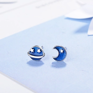 Asymmetric blue planet and moon stud earrings in silver-tone finish on a light blue background