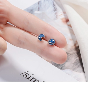 Close-up of blue enamel planet and crescent moon earrings held on fingers for size reference