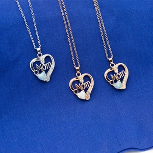 Silver, gold, and rose gold heart necklaces with opal and 'Mom' engraving on blue fabric