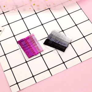 Close-up of glitter metal wave hairpins in pink and black gradients on white grid background