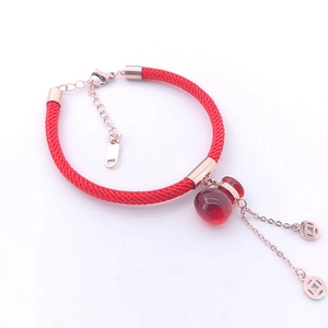 Detail of red braided bracelet featuring a rose gold chain and red gourd pendant charms