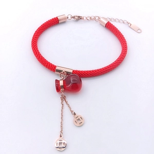 Detail of red braided lucky bracelet with money bag pendant and rose gold coin charms