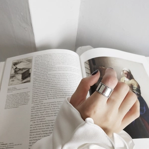 Close-up of wide silver ring with beaded edges worn on finger over an art book