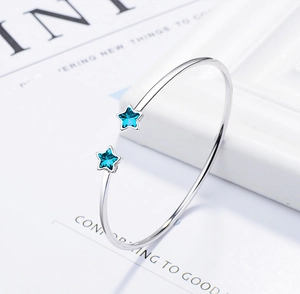 Close-up of silver open cuff bracelet with blue crystal stars on a white background