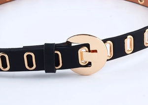 Macro detail of black PU leather belt featuring golden horseshoe buckle and metal eyelets