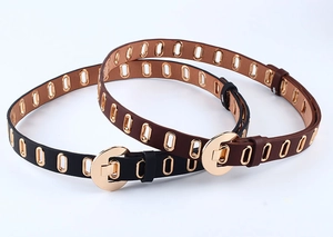 Detail of black and brown PU leather belts featuring all-over gold oval eyelet studs