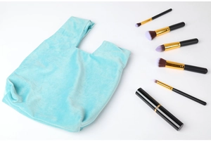 Flat lay of light blue velvet gift bag with makeup brushes on white background