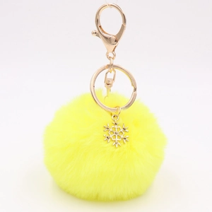 Macro detail of plush yellow pom-pom keychain with golden alloy snowflake charm