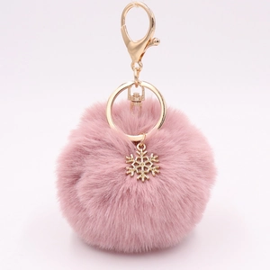 Detail view of a fluffy pink faux fur pompom keychain with a golden snowflake metal charm
