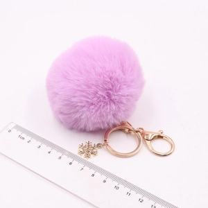 Close-up of purple plush pom-pom keychain with golden snowflake pendant and metal clasp
