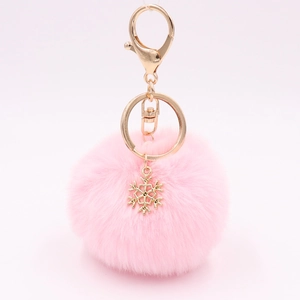 Detail of pink faux fur keychain with golden alloy snowflake pendant on soft background