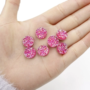 Detailweergave van 12mm roze hars cabochons met sprankelende minerale textuur op de hand