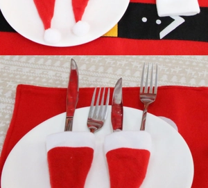 Mini red and white Santa hat cutlery holders on a white plate with Christmas tablecloth
