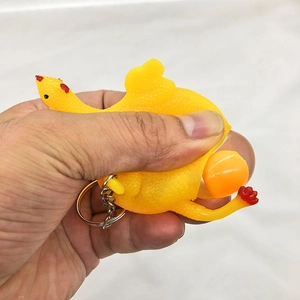 Macro detail of hand squeezing a yellow rubber chicken toy to pop out an orange egg ball