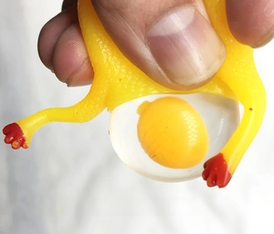 Close-up of a squeezing rubber chicken toy popping out a yellow egg yolk for stress relief