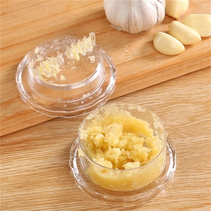 Manual transparent plastic garlic press and mincer on a wooden board with fresh cloves