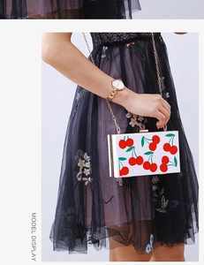 Detail of square cherry acrylic clutch bag with gold chain held by a model