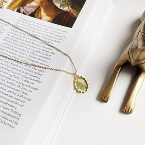 Detail of vintage gold oval textured pendant necklace on an artistic book background