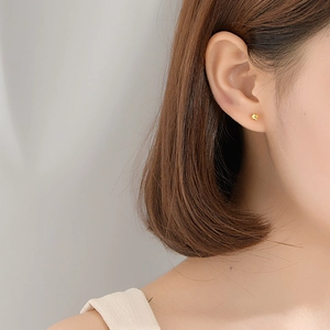 Minimalist tiny gold ball stud earrings for women shown worn in a stylish side view