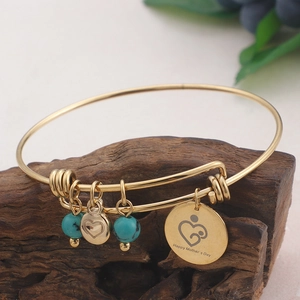 Golden Mother's Day bangle with blue beads and heart charm on a wooden base