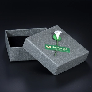 Gray textured paper jewelry box with white calla lily and heart sticker on black background