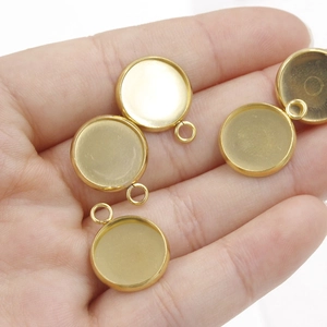 Golden stainless steel round pendant trays with small rings for DIY jewelry making in palm
