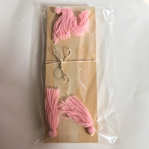 Detail of wooden wall shelf with pink yarn tassels and beige hemp rope bows
