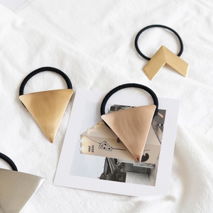 Golden geometric hair ties with brushed metal texture on a white linen surface