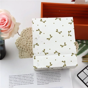 White paper gift bag with gold bow patterns and floral decor in a flat lay setup
