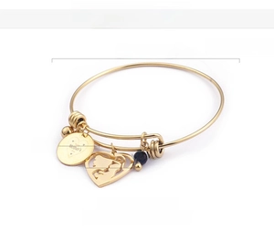 Macro detail of 18K gold bangle with Happy Mother's Day engraving and blue bead charms